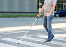 Człowiek niewidomy z białą laską przechodzi przez przejście dla pieszych