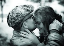 Zdjęcie przedstawia dziewczynę i chłopaka, chłopak całuje w czoło dziewczynę.