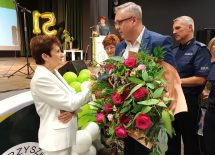Założycielka stowarzyszenia przyjmuje gratulacje i kwiaty od stojącego naprzeciw niej mężczyzny.